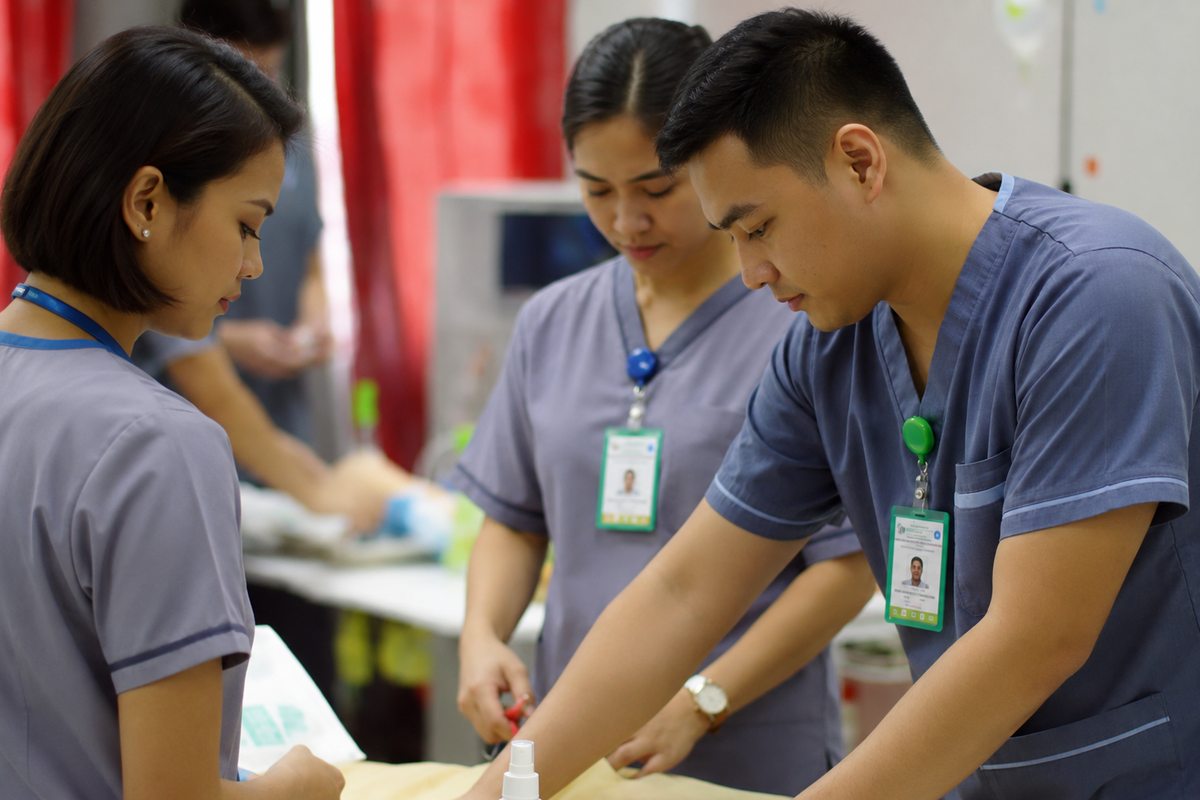 Three clinic nurses working together at a patient bedside.